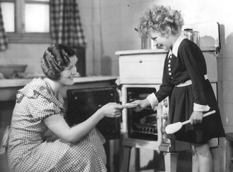An old black and white image of a mother and child using a Belling cooker 