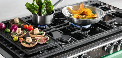 A gas cooktop being used with a frying pan, sauce pan and griddle plate all at the same time